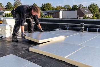 Isolatiemonteur brengt PIR-isolatieplaten aan op een plat dak